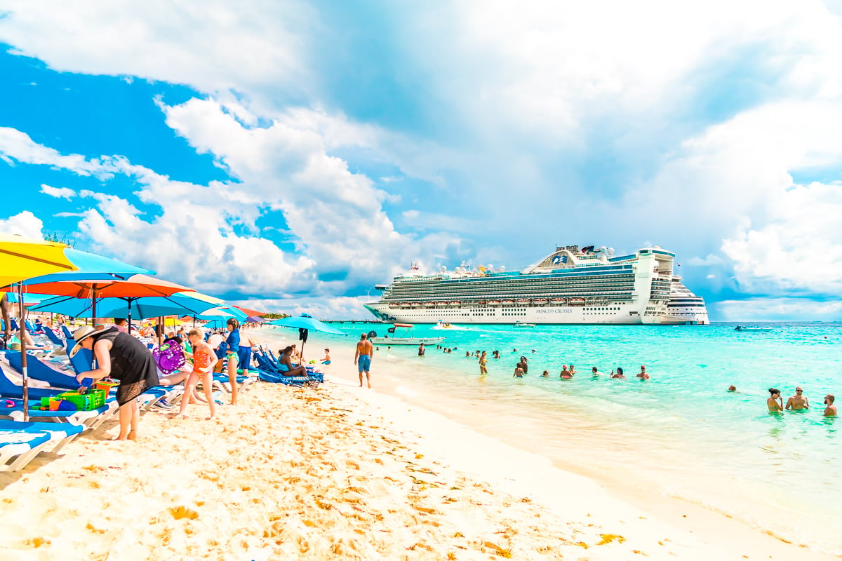 Caribbean Princess Cruise Ship in port in Grand Turk. Photo from the beach with people and colorful umbrellas.