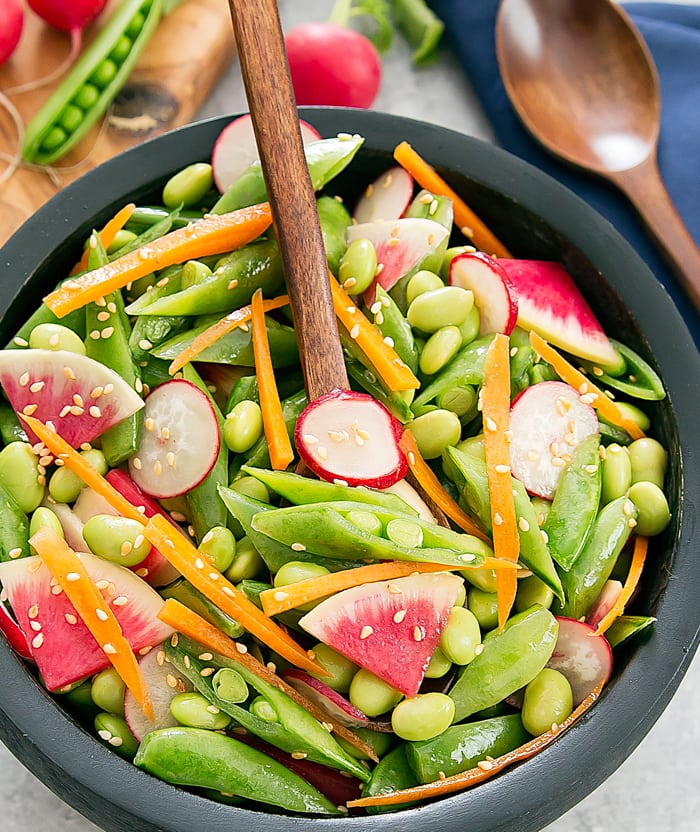 an overhead photo of a bowl of edamame snap peas sesame salad with a wooden spoon