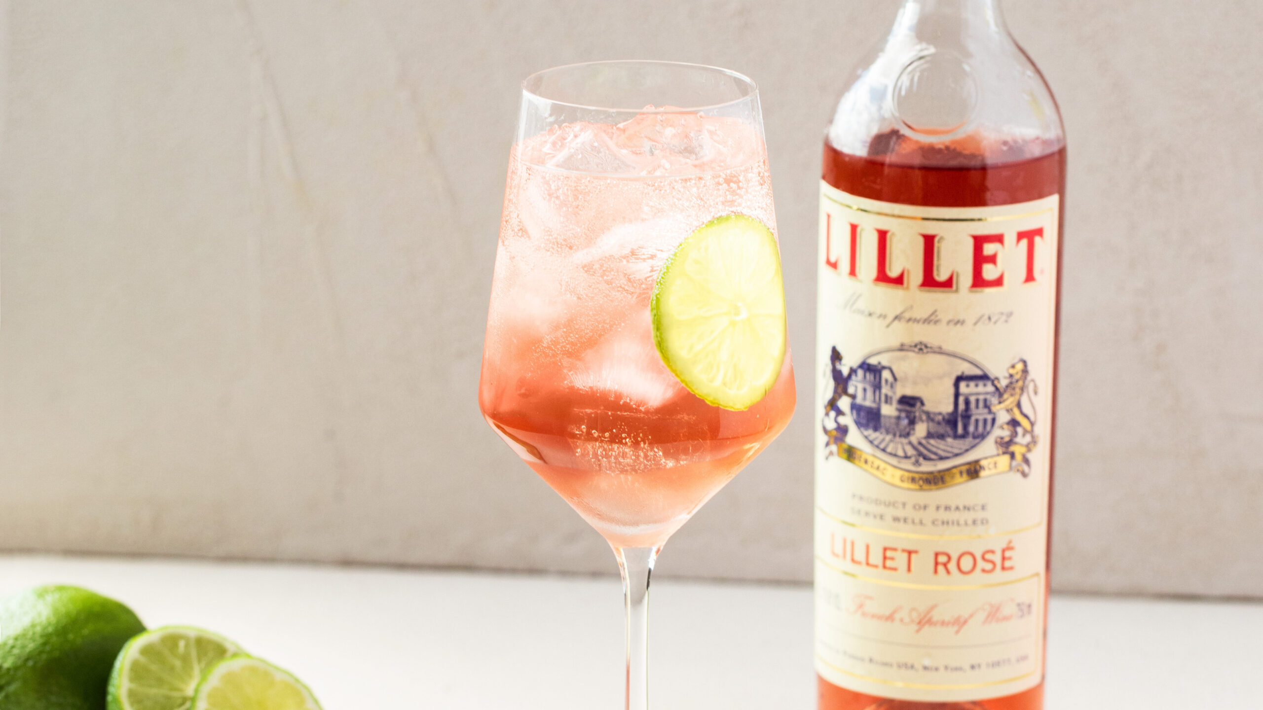 Lillet Rosé Spritz with slices of strawbery and cucumber with bottle of lillet in background