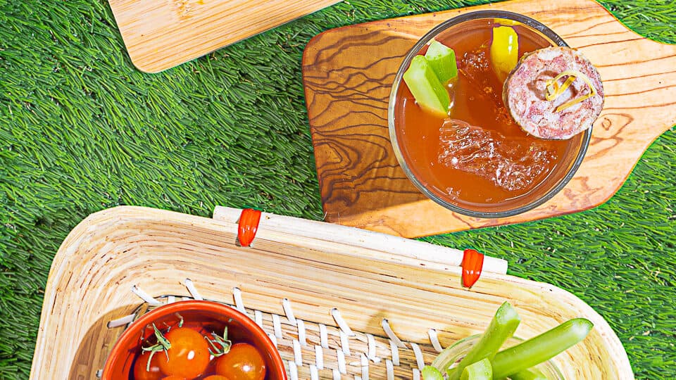 Top down view of bloody mary drink with garnishes on a green grass