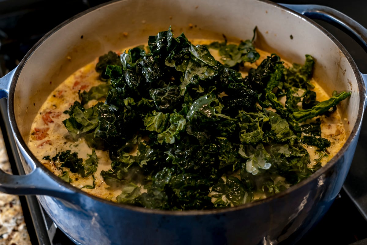kale added to pot of sausage and gnocchi soup.