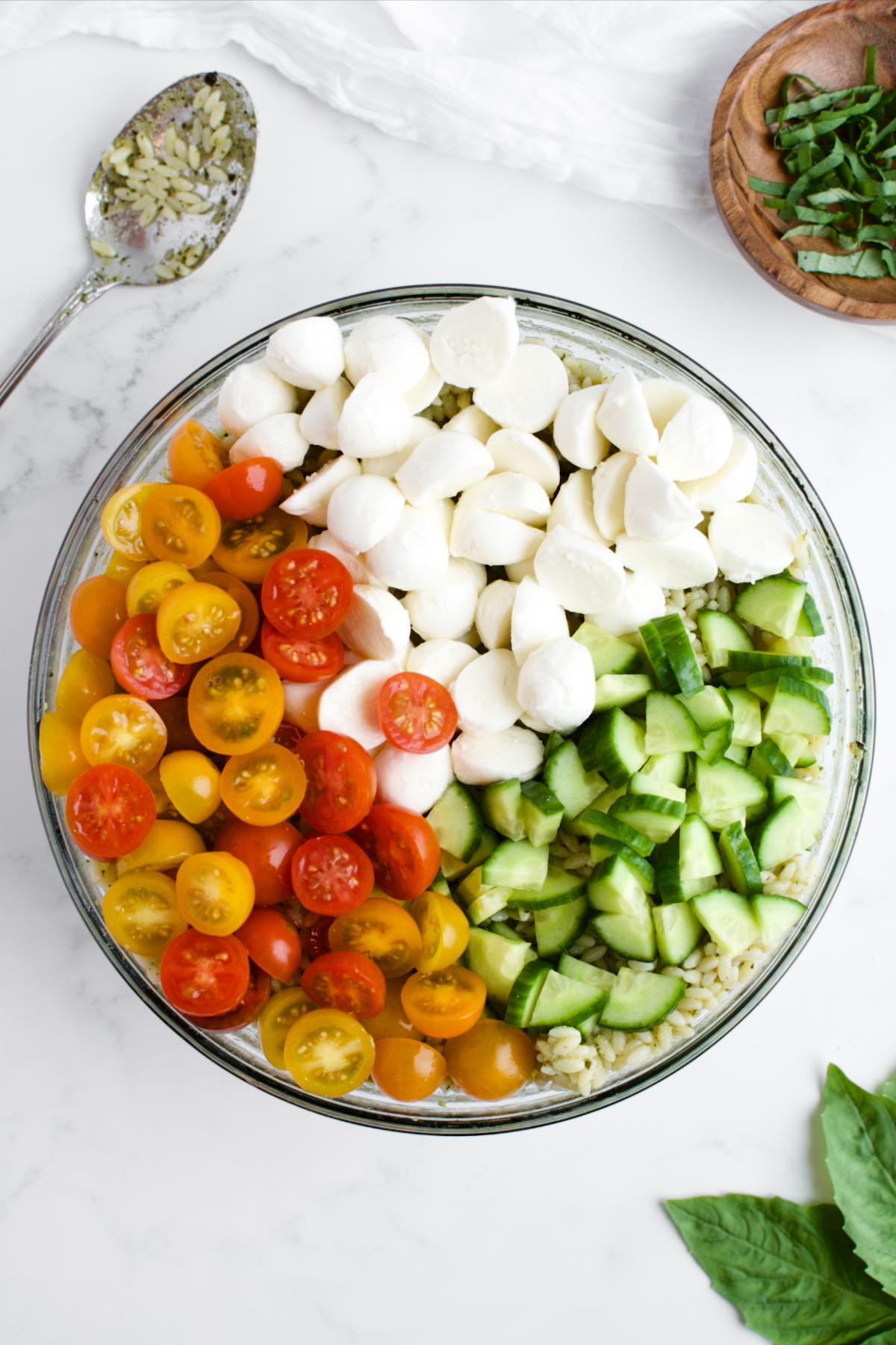 A glass bowl with layers of cucumber, tomatoes and mozzarella, not yet stirred together.