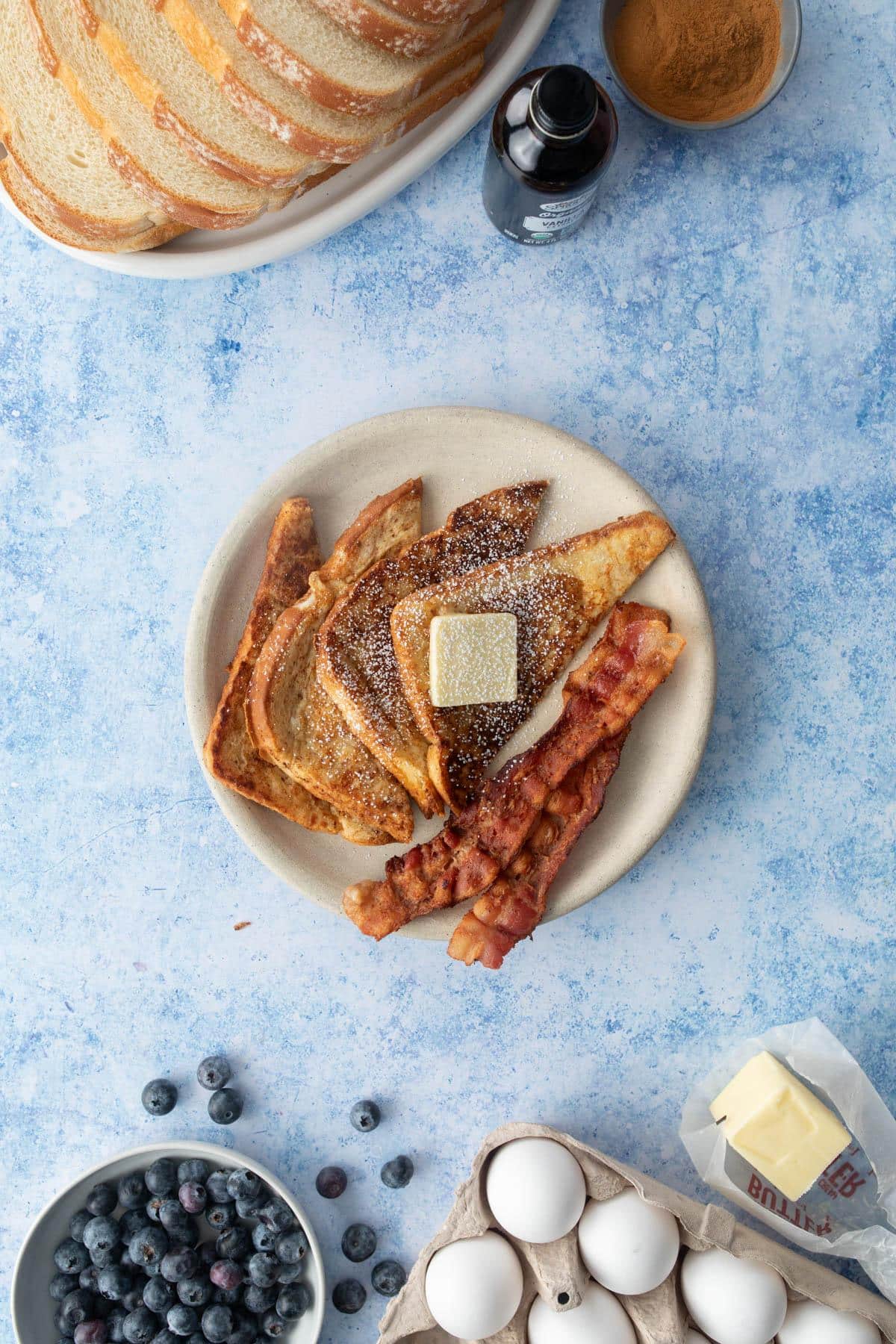 four slices french toast with butter and bacon on plate