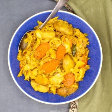 Tikil gomen, Ethiopian cabbage, carrots and potatoes, in blue bowl with spoon.