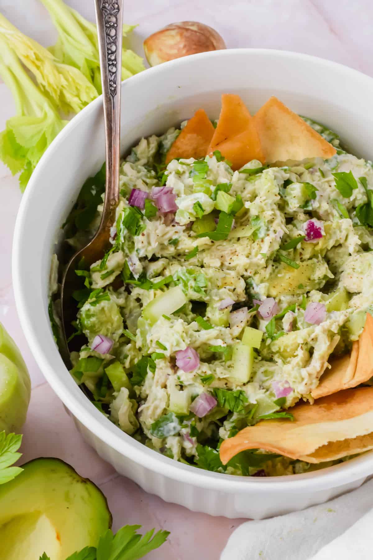 Close up view of creamy avocado greek yogurt chicken salad in a bowl with a spoon garnished with pita chips