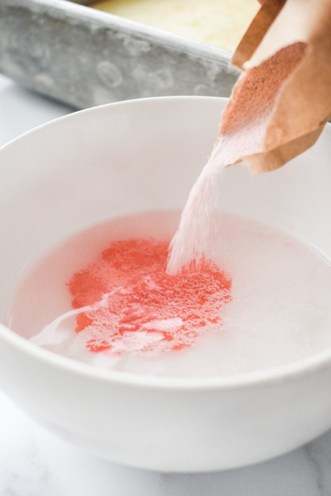 pink gelatin powder being poured into a bowl of hot water 