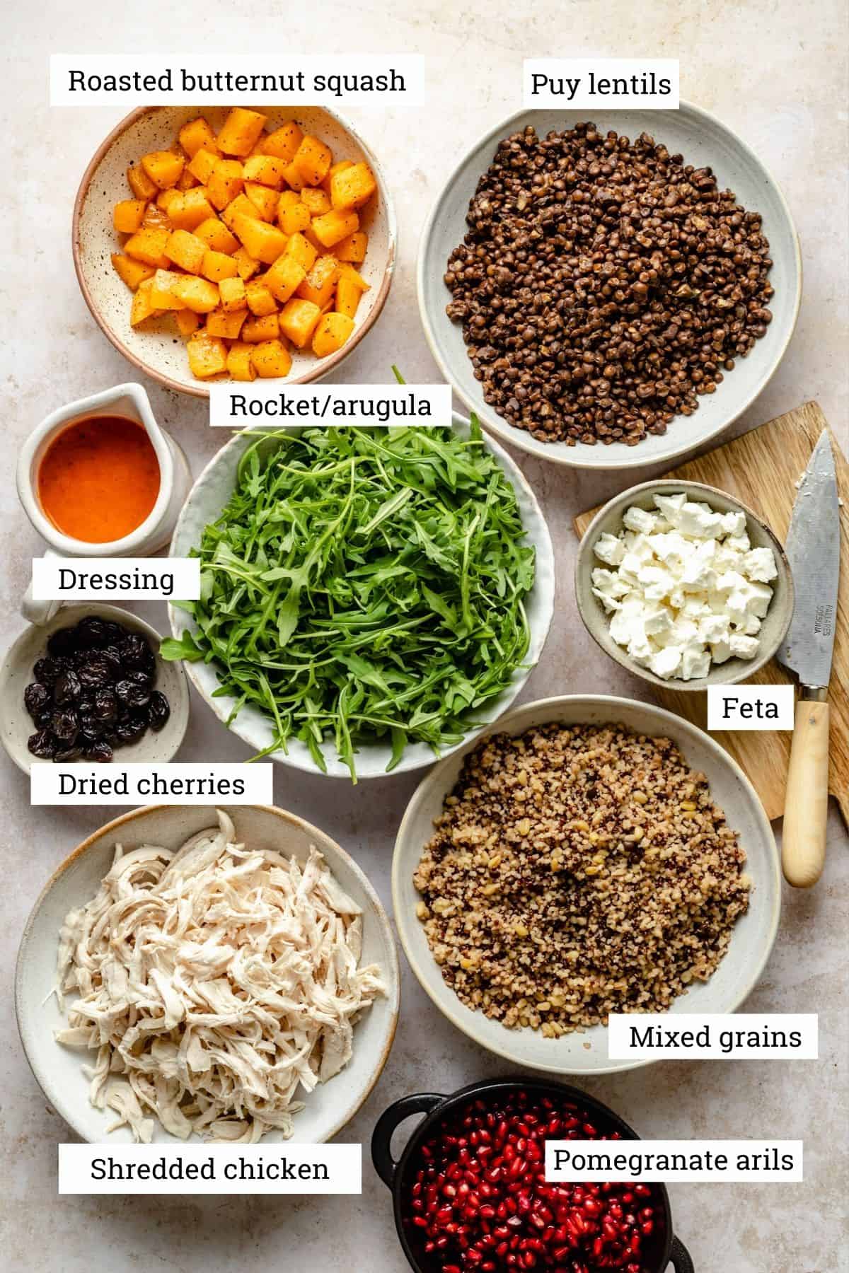 All the main ingredients for the fall grain salad in various bowls including, grains, lentils, rocket, butternut squash and shredded chicken.