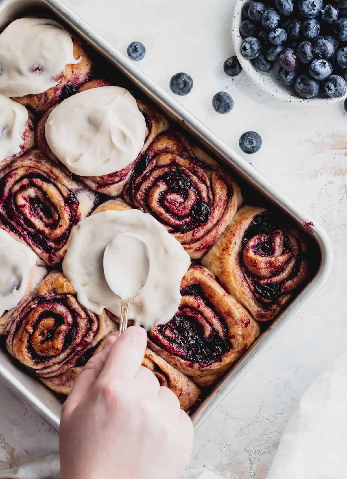 Spreading icing on top of blueberry cinnamon rolls.