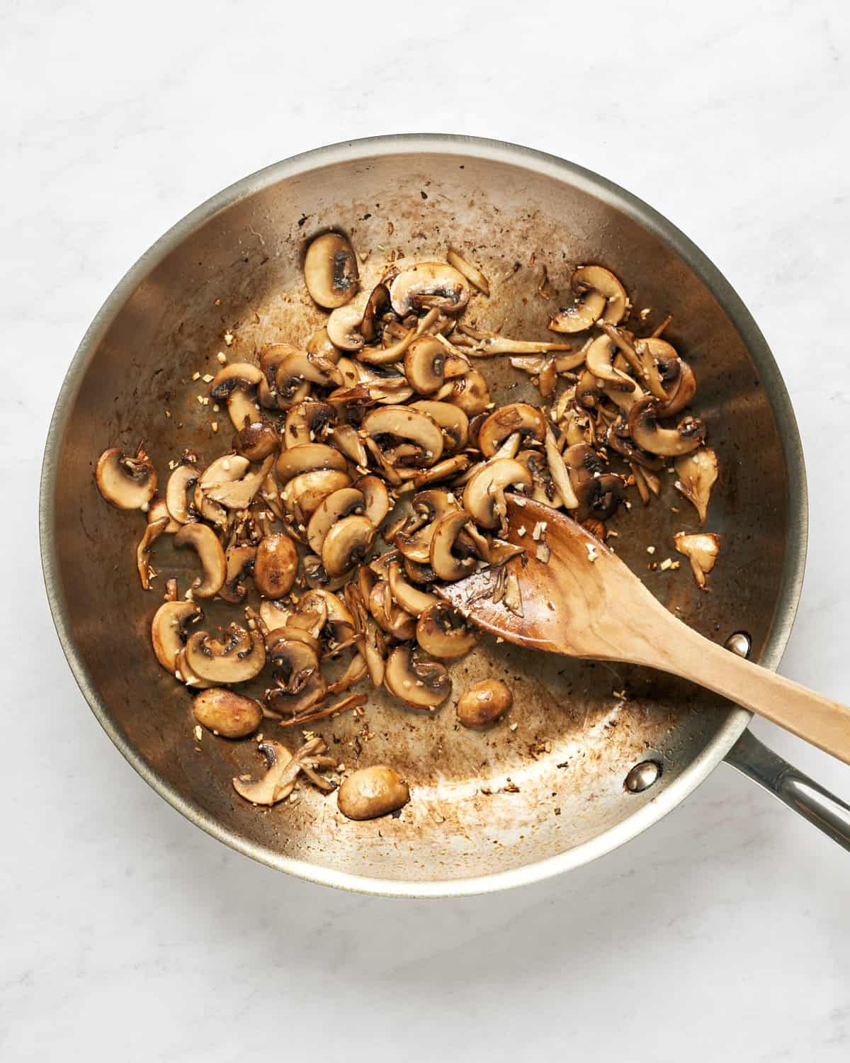 Sauteed mushrooms in 12-inch skillet with wooden spoon on marble background