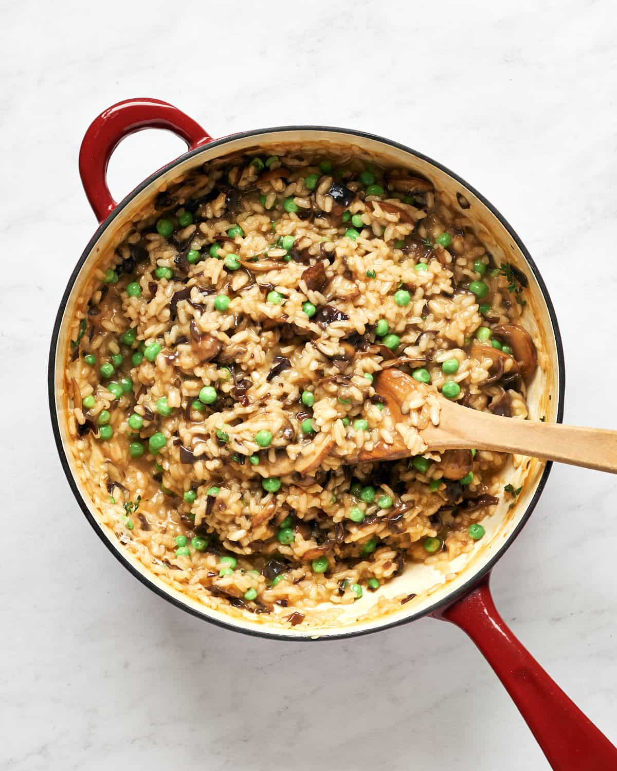 Stirring vegan mushroom risotto with peas in saucepan on marble background