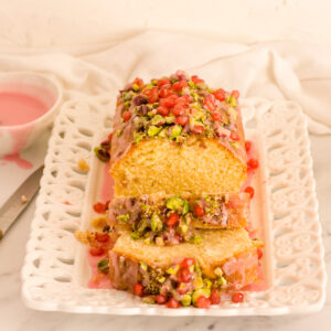 lemon pomegranate cake sliced with glaze in the background featured