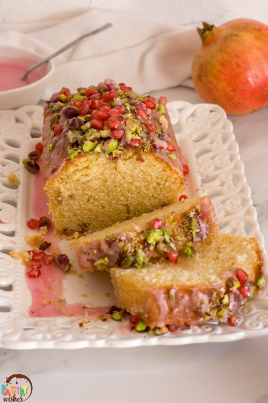 lemon pomegranate cake sliced with glaze and pomegranate in the background