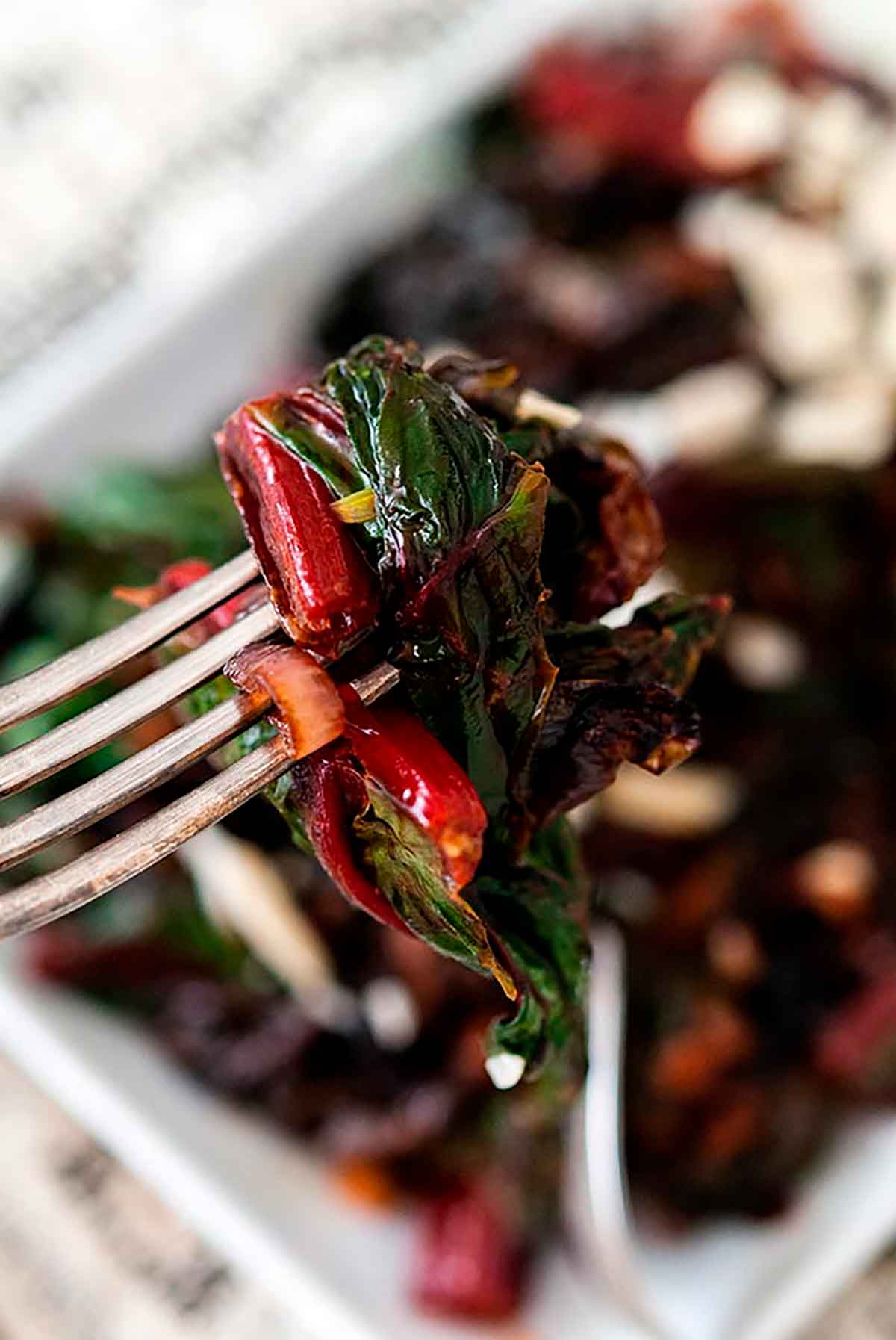 A fork with sautéd Swiss chard and caramelized shallots above a bowl of Swiss chard.