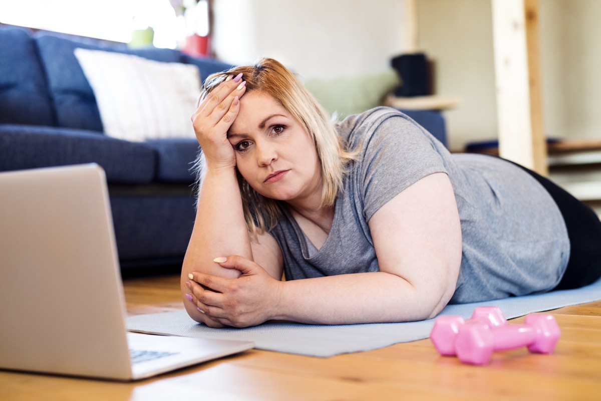 overweight woman at home lying on the floor, laptop in front of her, prepared to work out on mat according to video