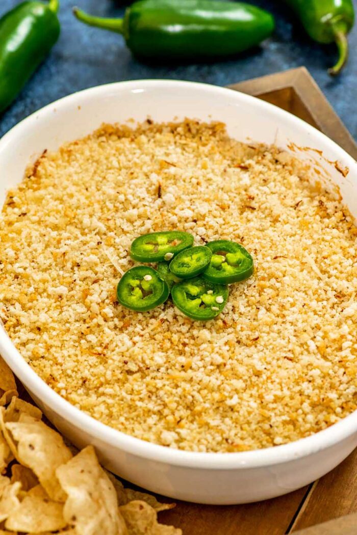 Side view of a fully baked dish of jalapeno popper dip, topped with a few fresh slices of jalapeno.