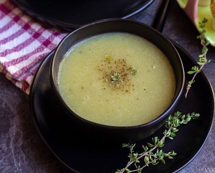 cream of zucchini soup in black bowl with thyme on the side