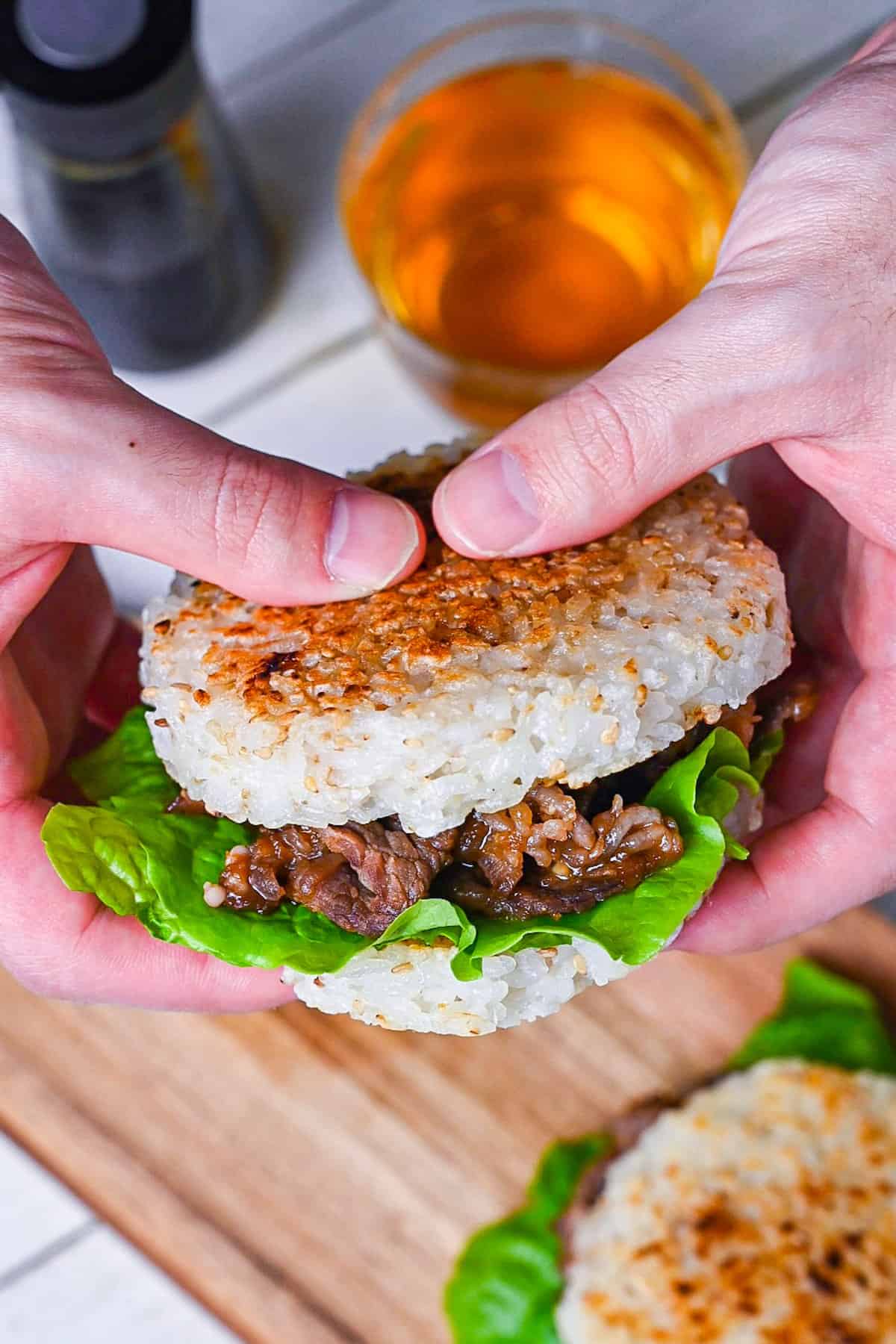 Yakiniku Rice Burger filled with frilly lettuce and yakiniku style pan fried beef on a wooden chopping board