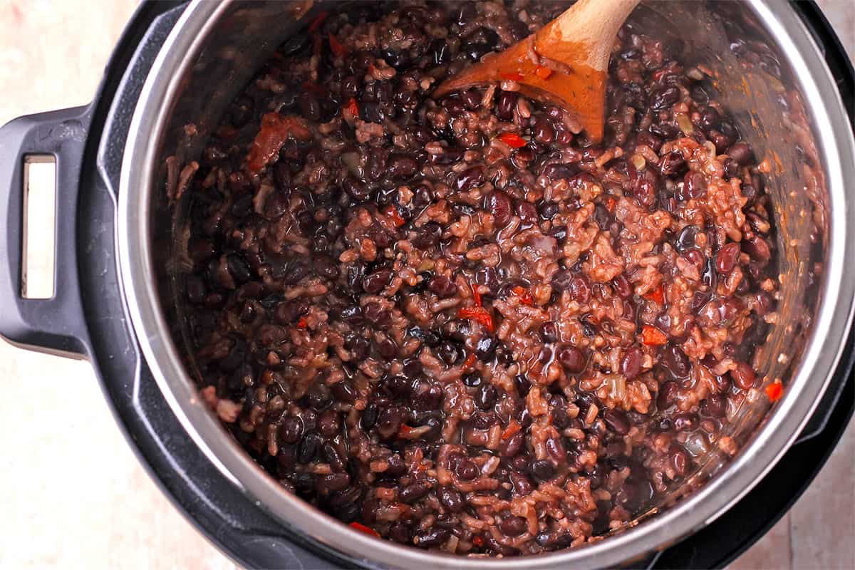 An Instant Pot with black beans risotto with a wooden spoon.