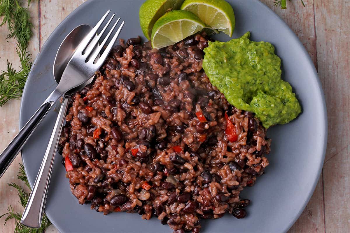 A blue plate with black beans risotto with guasacaca sauce and a fork and spoon.