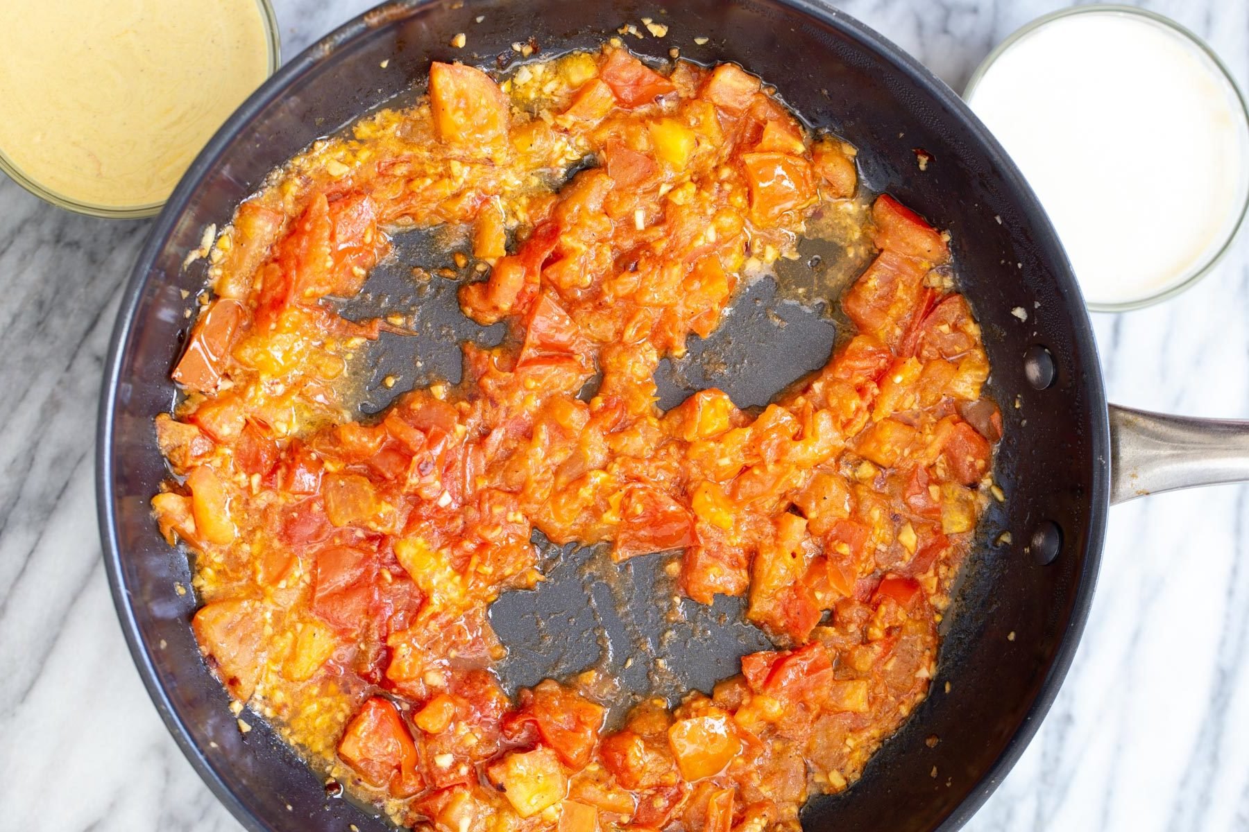 tomato sauce in a sauteeing pan being pushed aside to make room for tofu eggs