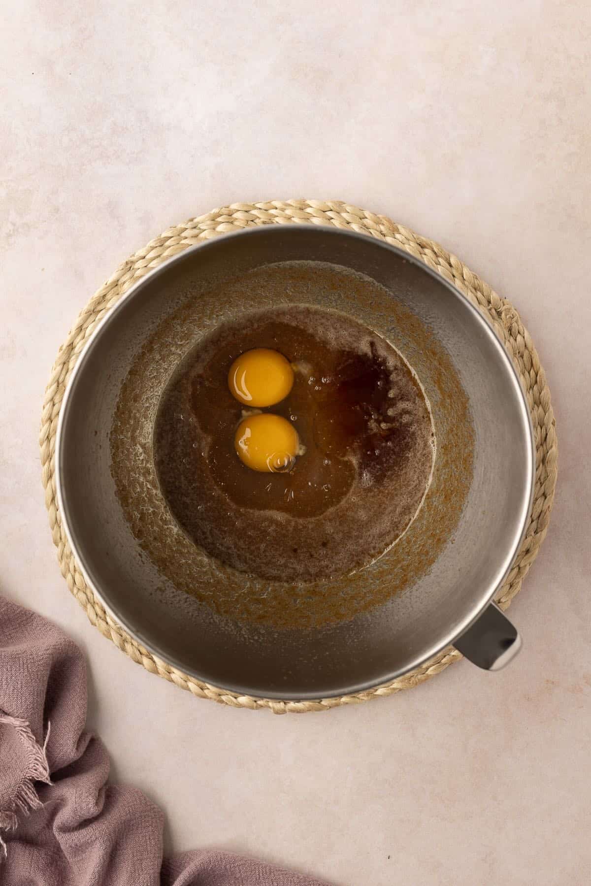 Two raw eggs added to butter and sugar in a metal mixing bowl. 