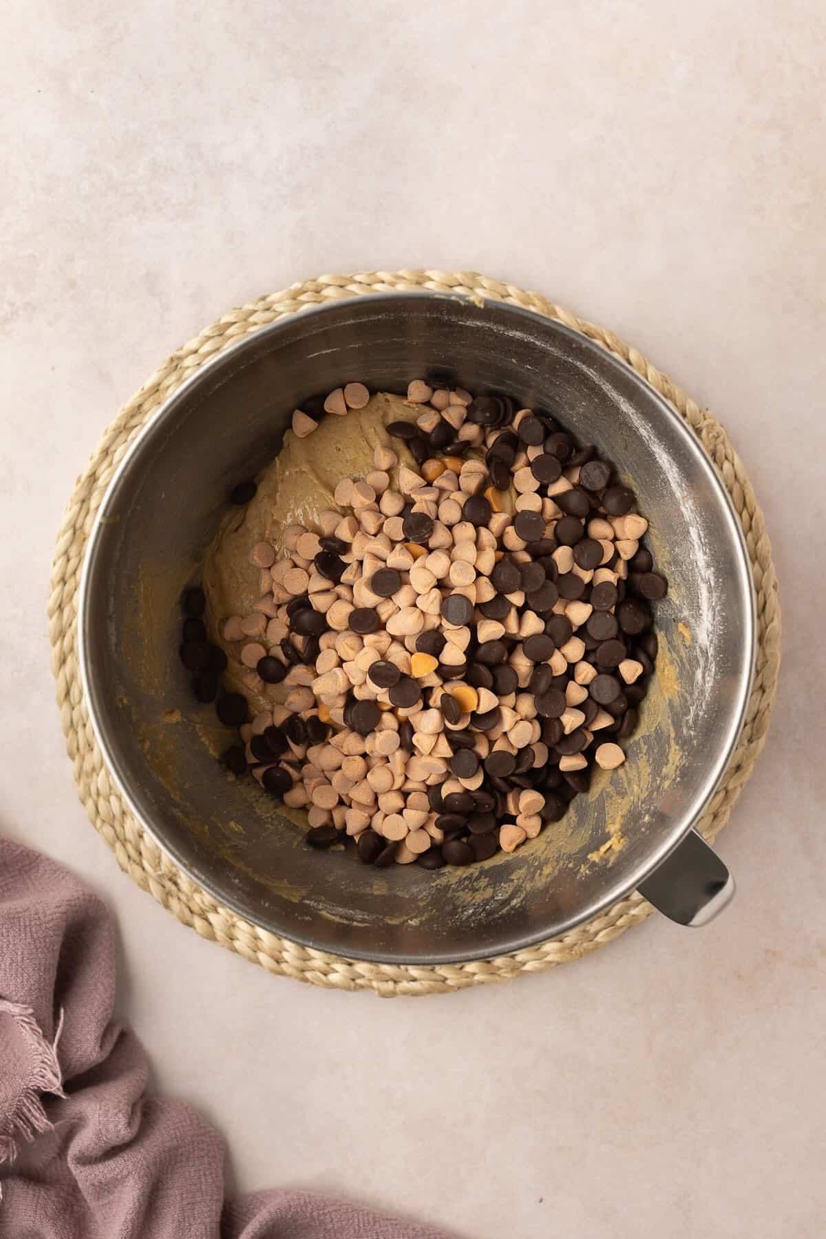 Chocolate and butterscotch chips added to cookie dough in a metal mixing bowl. 