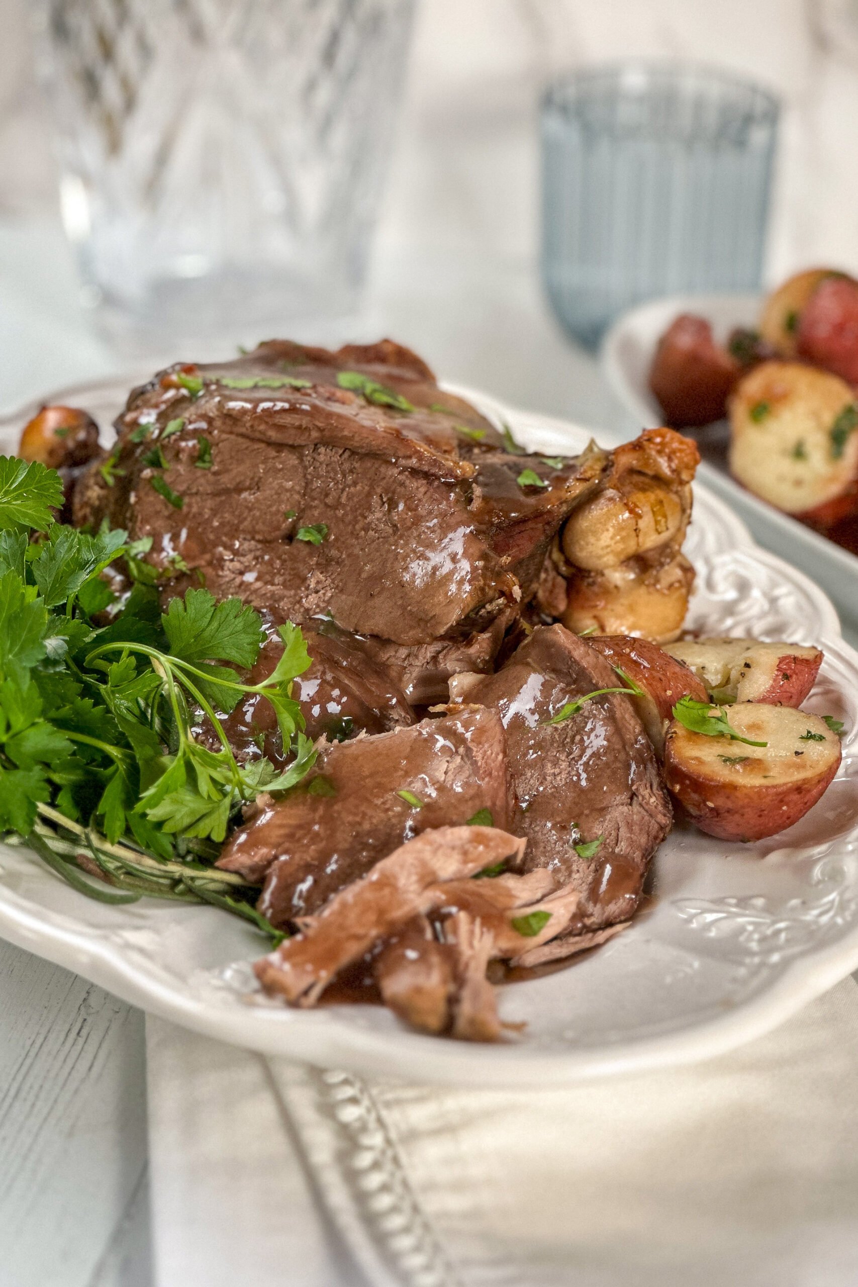 Side view of sliced Lamb Roast with fresh herbs and gravy.
