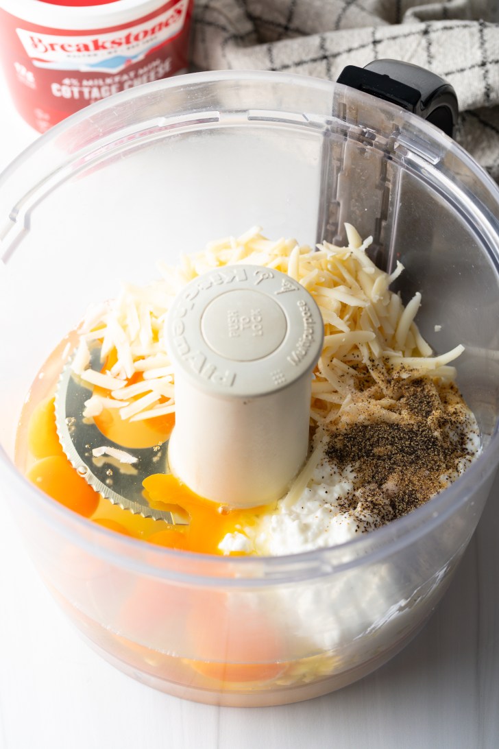 Shredded cheese, cottage cheese, eggs, and spices in a food processor.