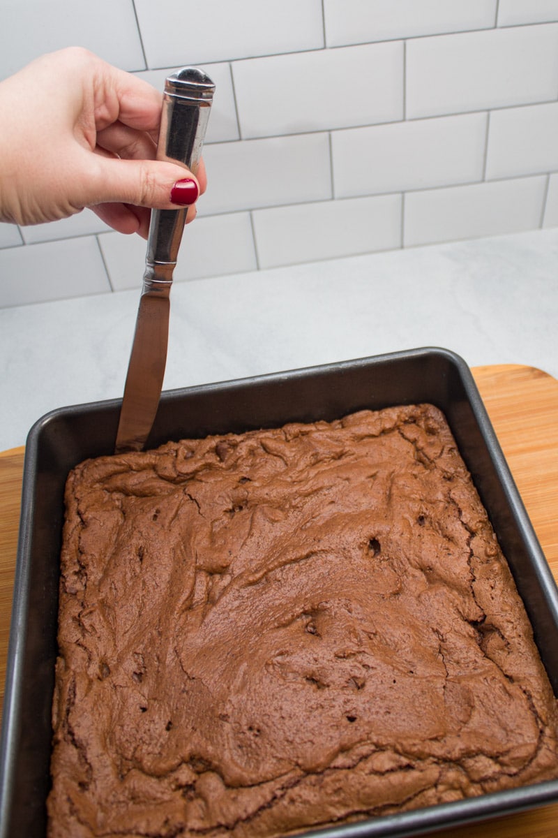 Using a knife to loosen the edges of a pan of espresso chocolate chip brownies.