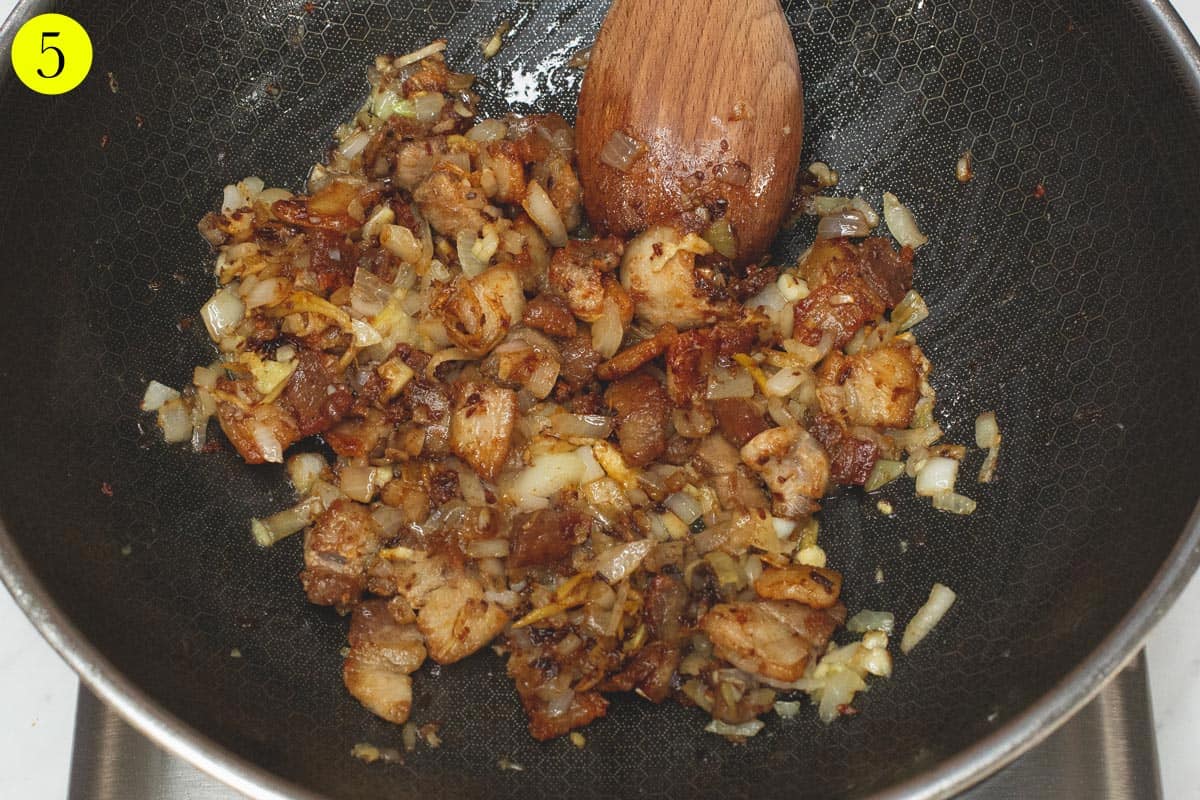 Sauteing pork and aromatics with shrimp paste in a wok.