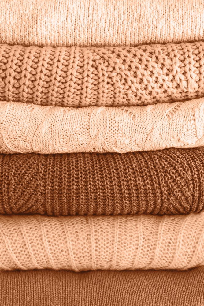 Stack of warm cozy blankets in different textures.  Image toned in trendy color of year 2024 Peach Fuzz. Closeup.