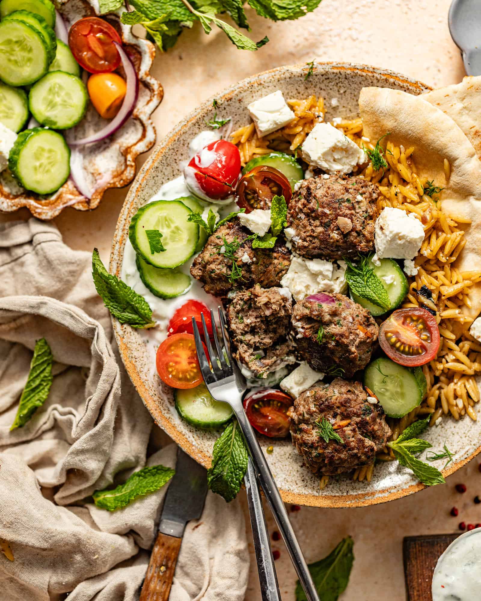 greek meatballs and orzo in a bowl with cucumbers, tomatoes, feta, and pita bread.