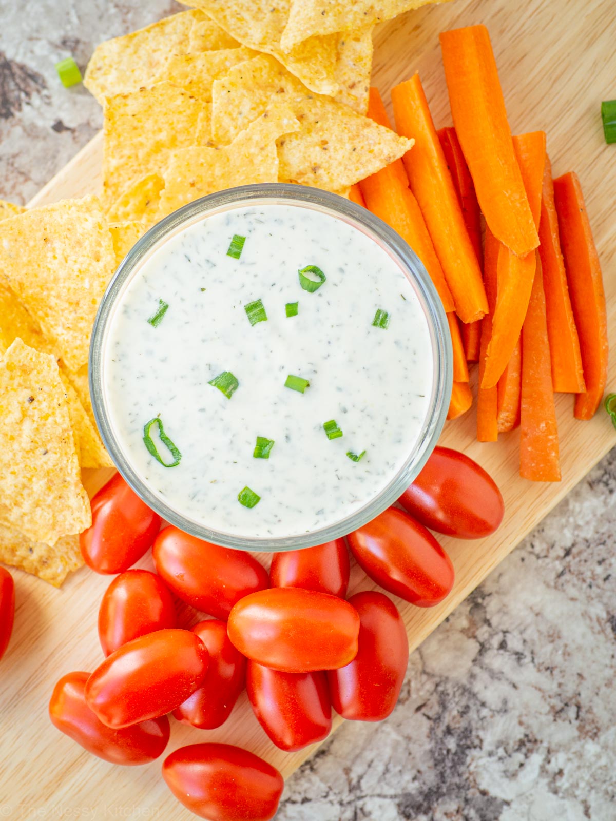 Bowl of ranch on a platter with vegetables and tortilla chips.