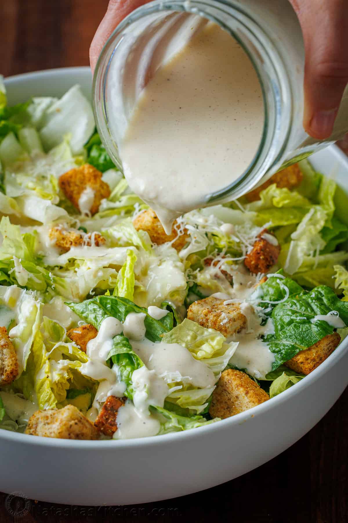 Pouring creamy caesar dressing over salad