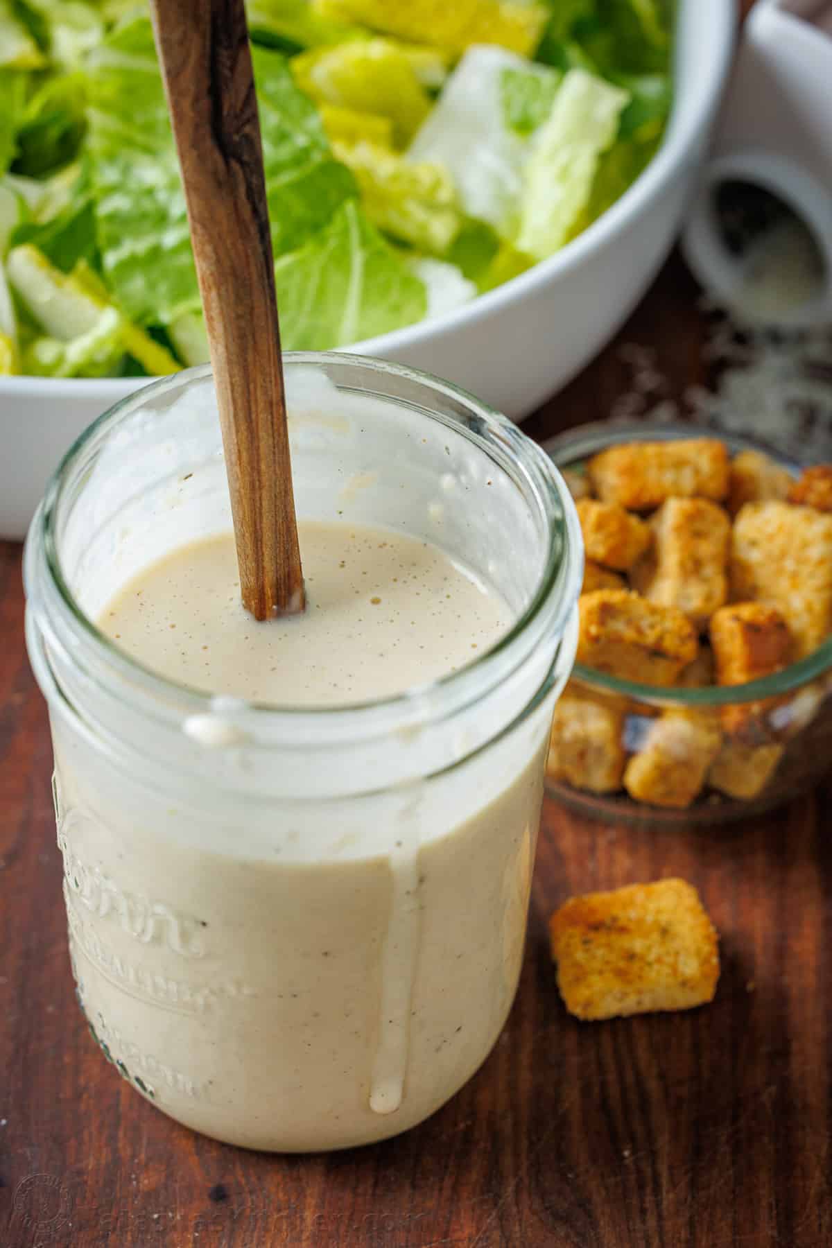 Homemade Caesar salad dressing in a jar with croutons and romaine lettuce