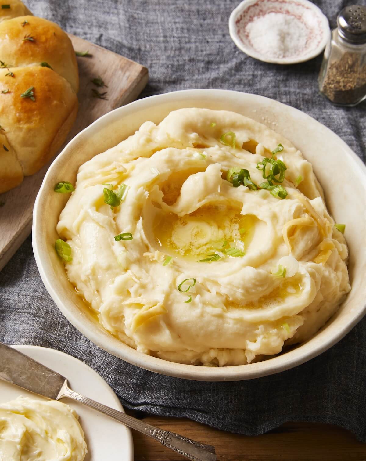 bowl of mashed potatoes with butter on a linen covered table.