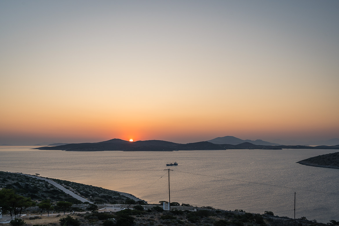 Panoramic view of sunrise over Schinnousa. A commercial ferry is sailing on the sea between Schinoussa and Iraklia Island.