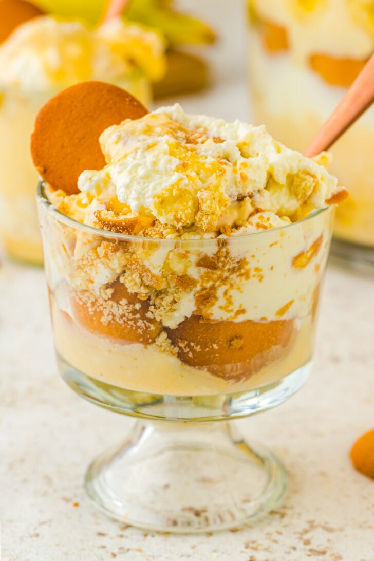 Banana pudding in a small serving glass perfectly layered to the top with a vanilla wafer cracked on the edge like a lime.
