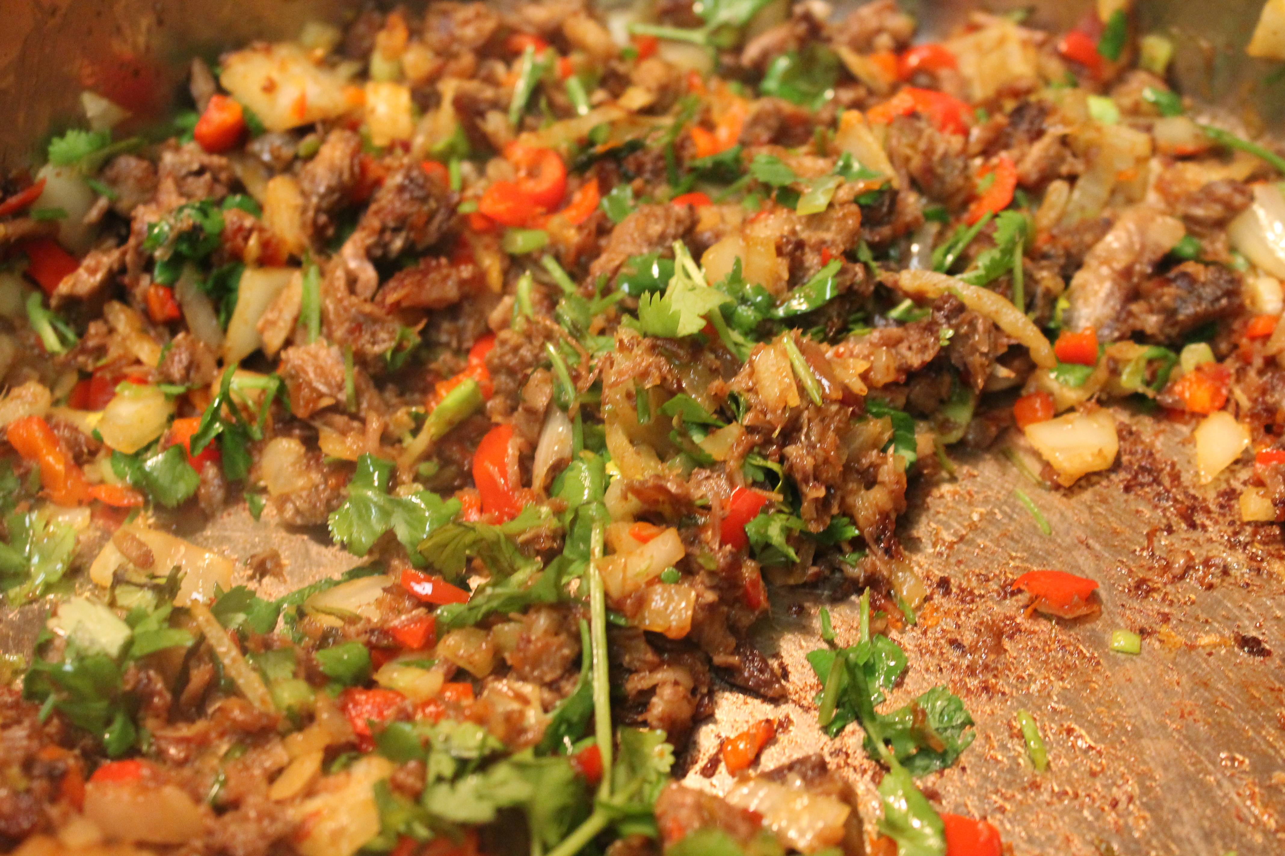 A closeup image of brisket, vegetables, and herbs sauteing in a skillet.
