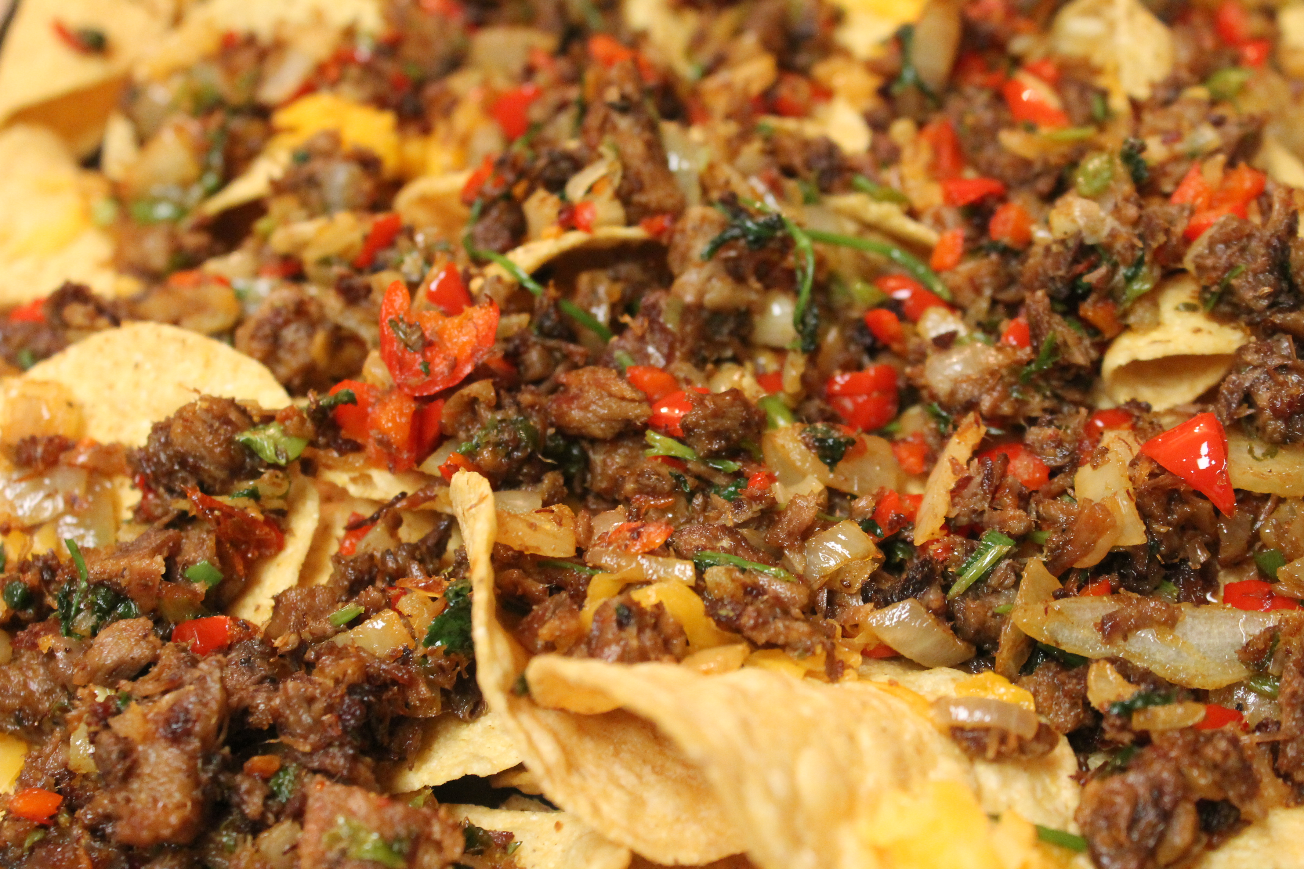 A closeup image of brisket, peppers, and onions spread over a layer of tortilla chips. These flavorful brisket nachos are almost ready for the oven!