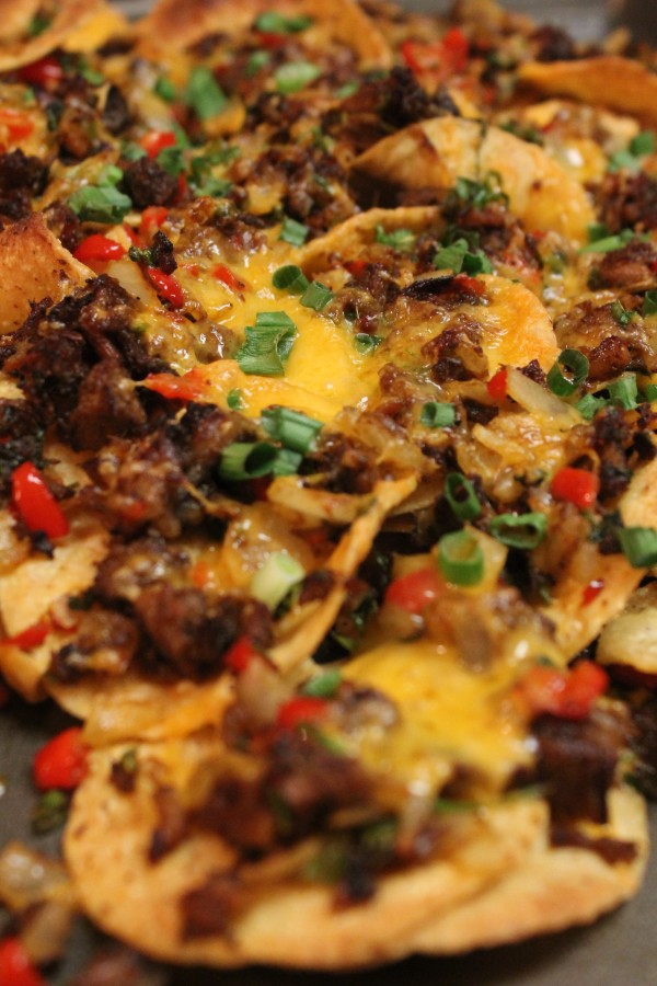 A closeup image of homemade brisket nachos topped with melted cheese, peppers, and onions.