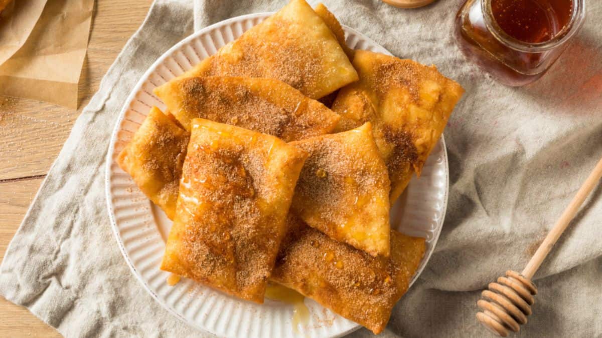 Plate of fried sweet cheese wontons sprinkled with sugar, served with a side of honey.