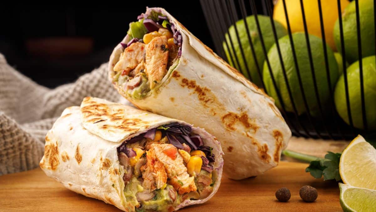 Chicken wrap with fresh vegetables and avocado on a wooden table.