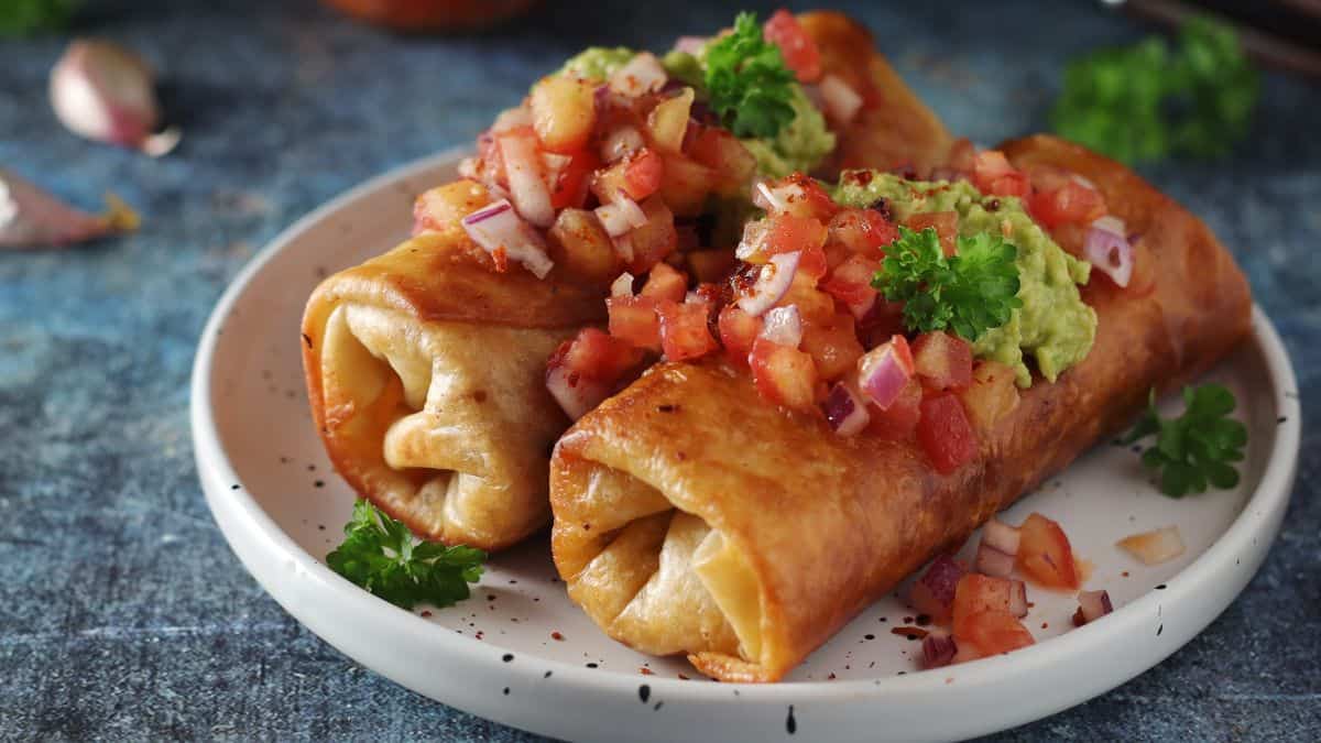 Plate of crispy taquitos topped with fresh salsa and guacamole.