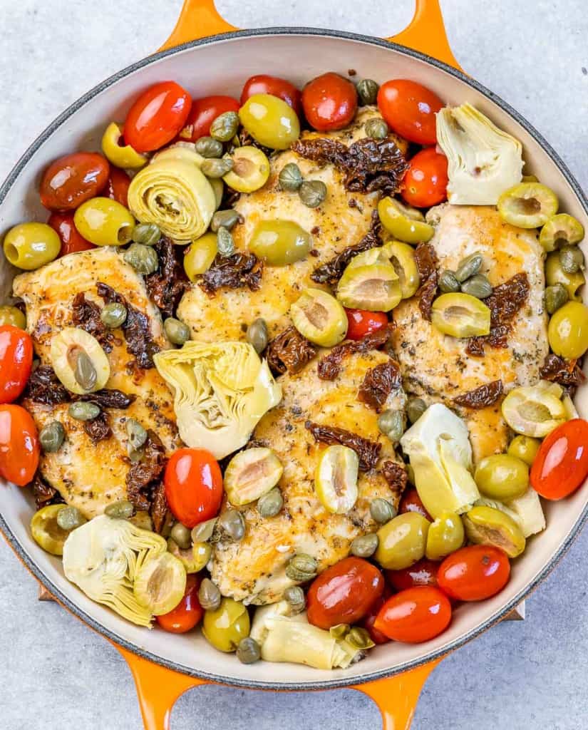 Chicken in a skillet with cherry tomatoes, artichokes and olives.