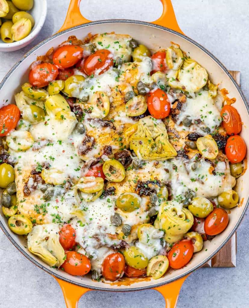 Melted cheese over chicken in a skillet with vegetables.