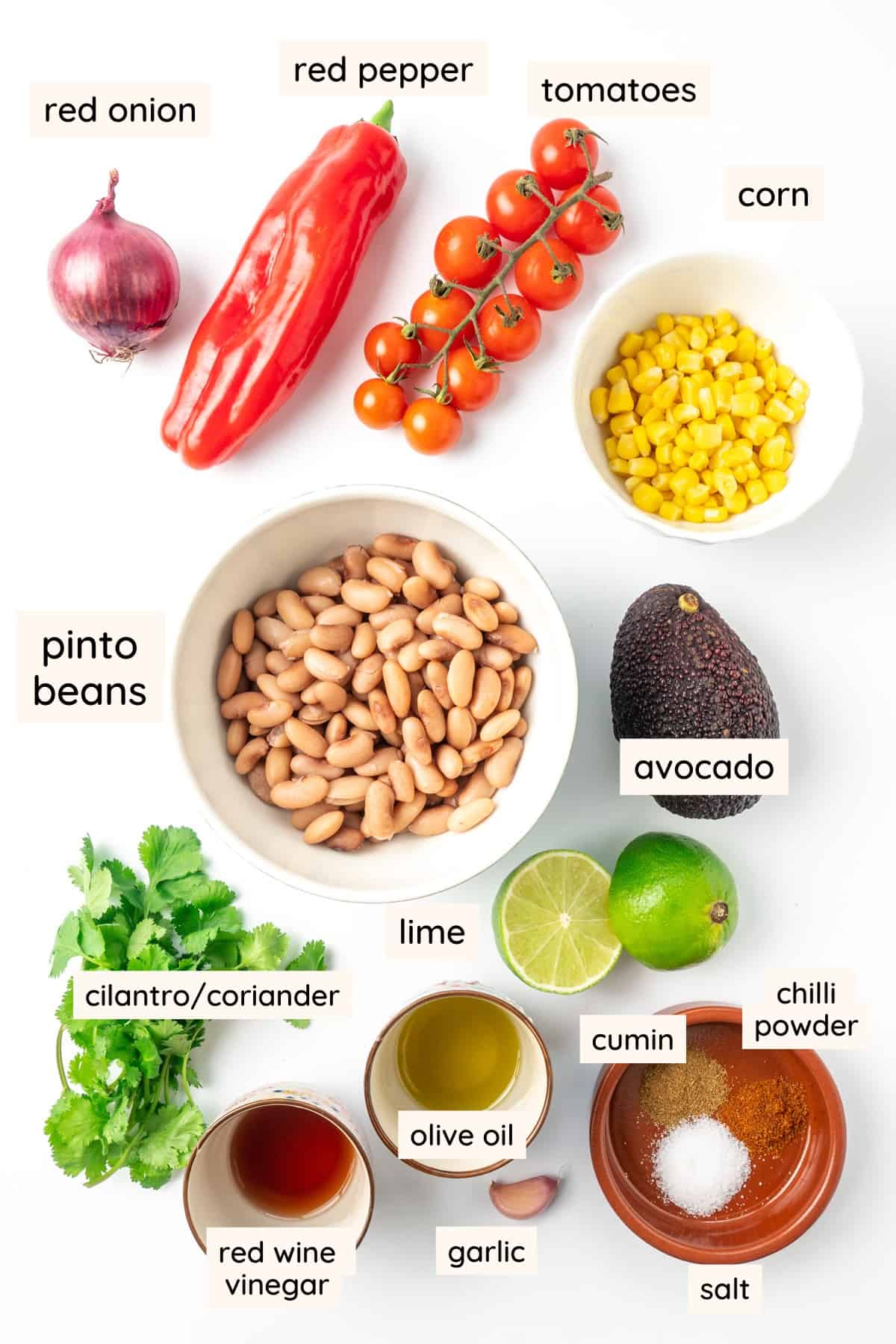 Ingredients of pinto bean salad: Cooked pinto beans, a red onion, an avocado, a red pepper, cherry tomatoes, sweetcorn, fresh cilantro, a lime, olive oil, red wine vinegar, a clove of garlic, ground cumin, chilli powder, and salt.