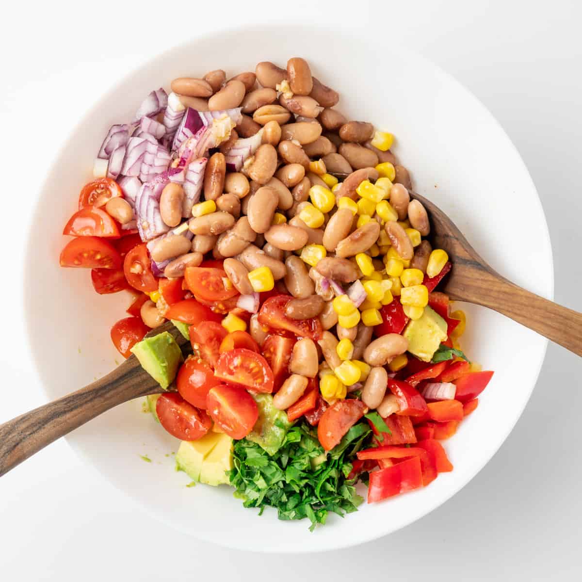The beans and vegetables are combined with the dressing and stirred through to make the salad.