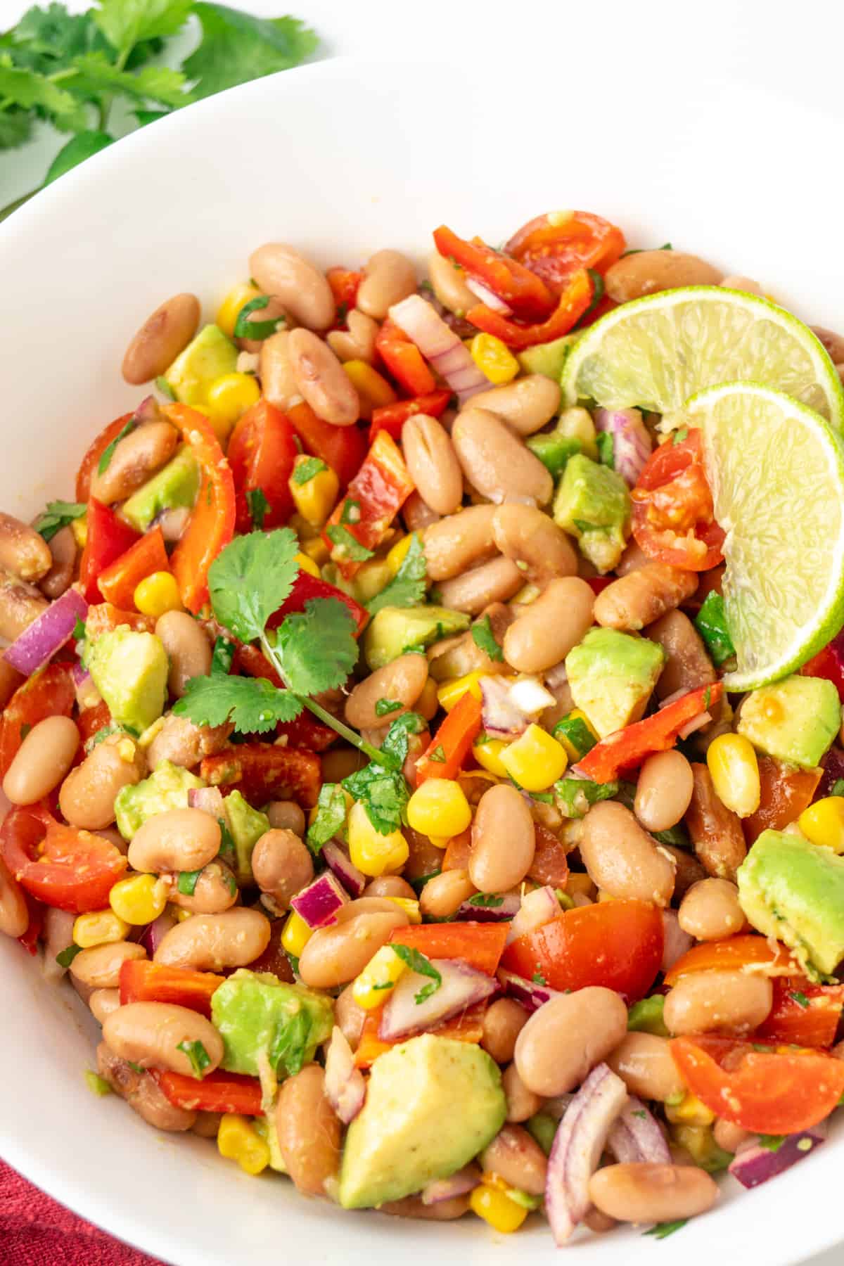 A colourful salad of beans and raw vegetables, garnished with lime wedges.