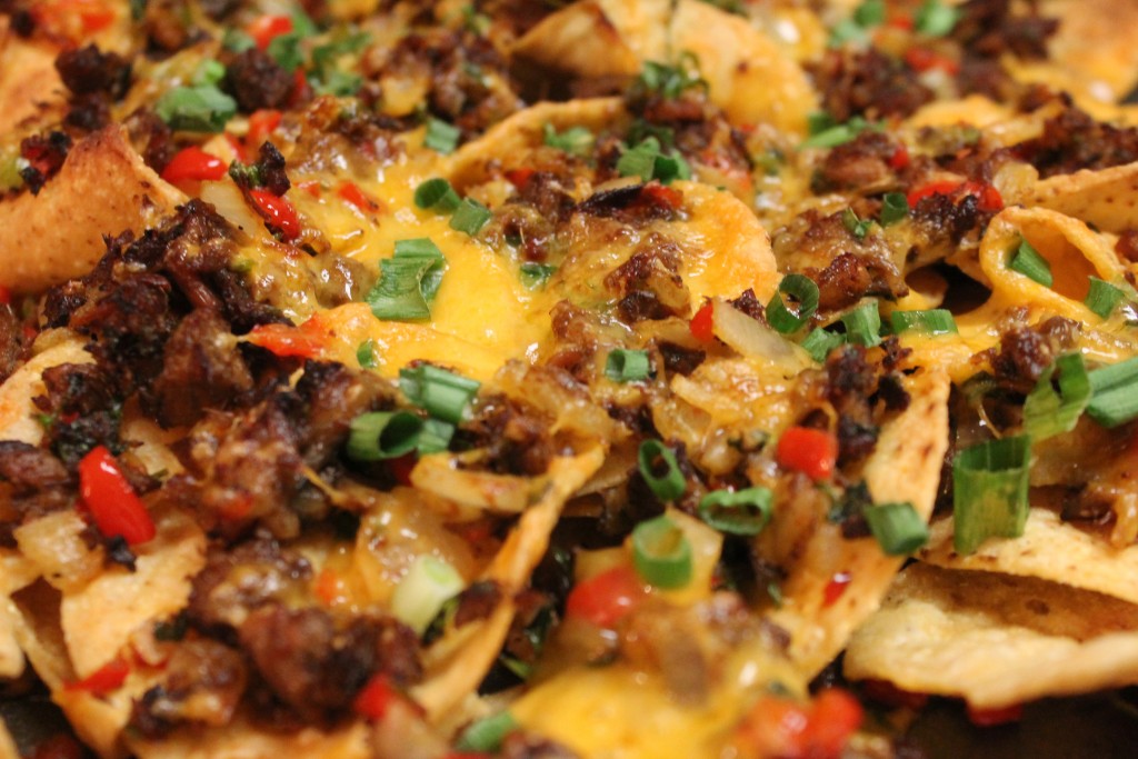A closeup image of brisket nachos on a pan, topped with a mixture of peppers, onions, and cilantro with leftover beef brisket.